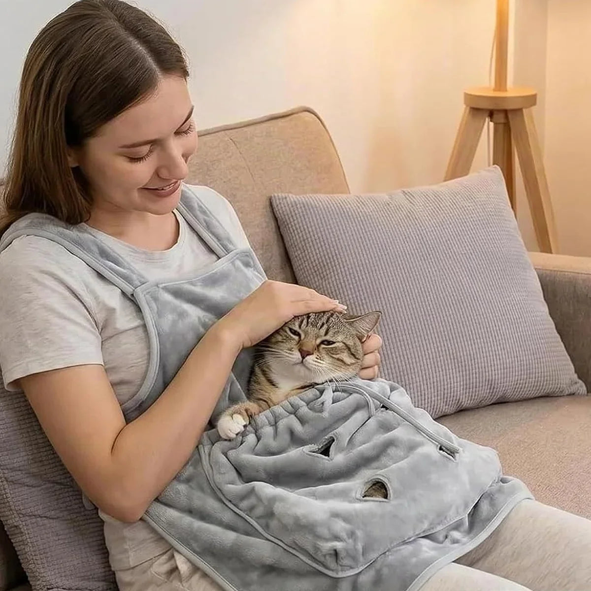 Calm tabby cat resting in the grooming apron pouch on a sofa